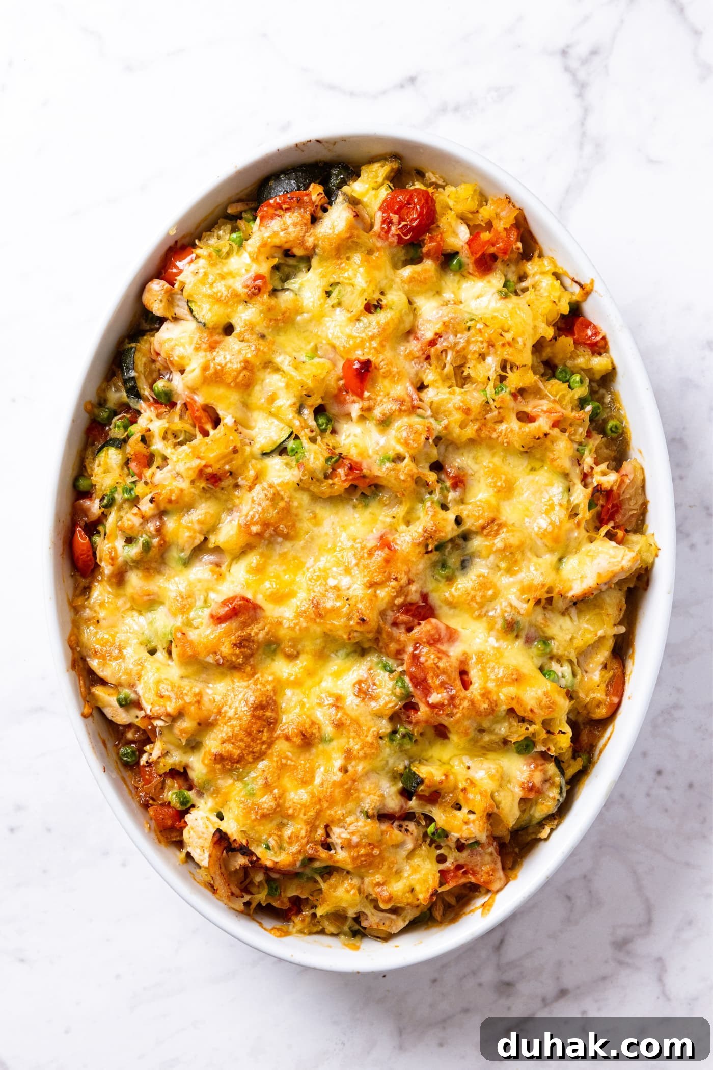 Cheesy Turkey & Spaghetti Squash Casserole Recipe 20 White oval baking dish sitting on marble surface right after coming out of the oven with melted cheese all over the top of spaghetti squash chicken casserole.