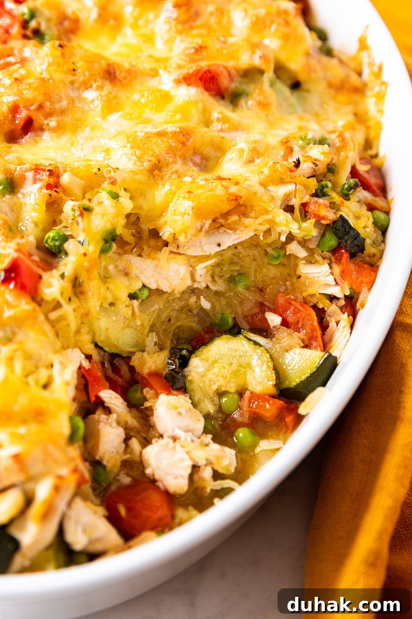 Cheesy Turkey & Spaghetti Squash Casserole Recipe 3 White oval baking dish filled with baked spaghetti squash chicken casserole with vegetables sitting in space from spoonful removed.