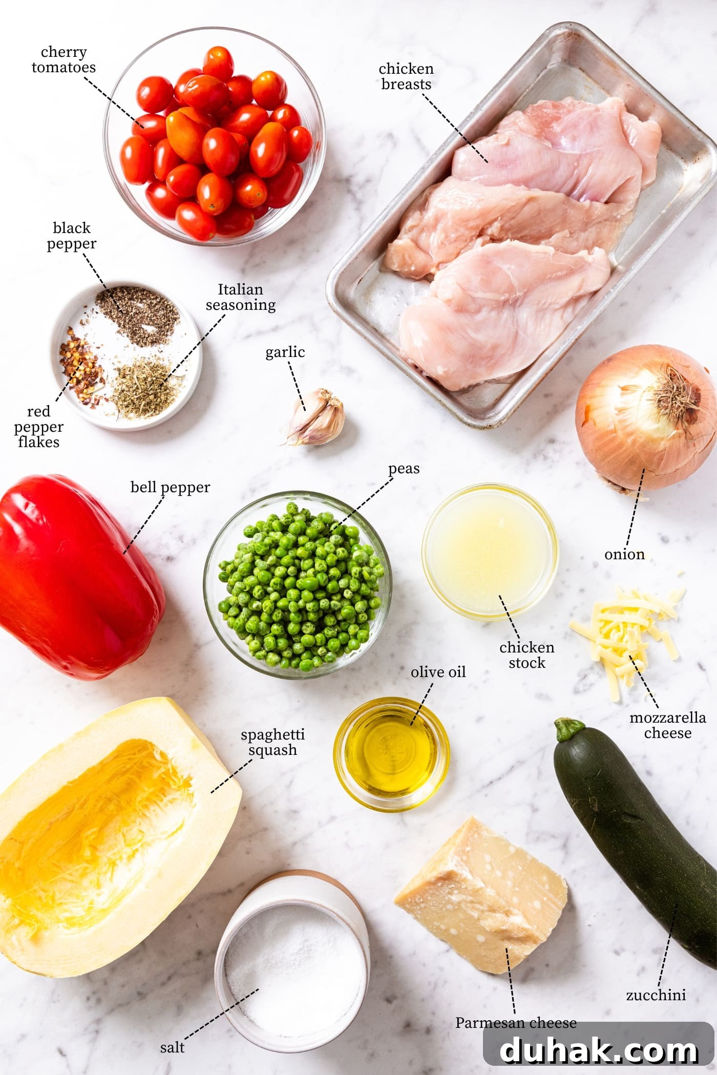 Cheesy Turkey & Spaghetti Squash Casserole Recipe 4 White marble surface filled with ingredients needed to make a casserole including spaghetti squash, bell pepper, peas, zucchini, onion, chicken, spices, and more.
