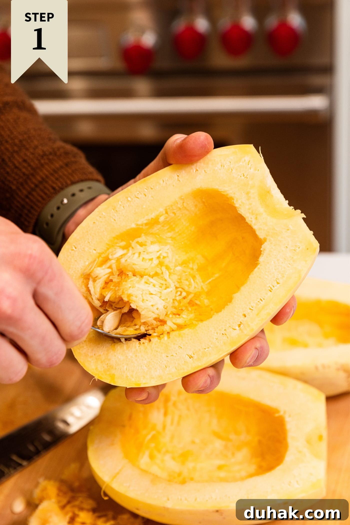 Cheesy Turkey & Spaghetti Squash Casserole Recipe 5 Hand holding spaghetti squash cut in half using a spoon to scoop out the interior flesh and seeds with more squash in background.