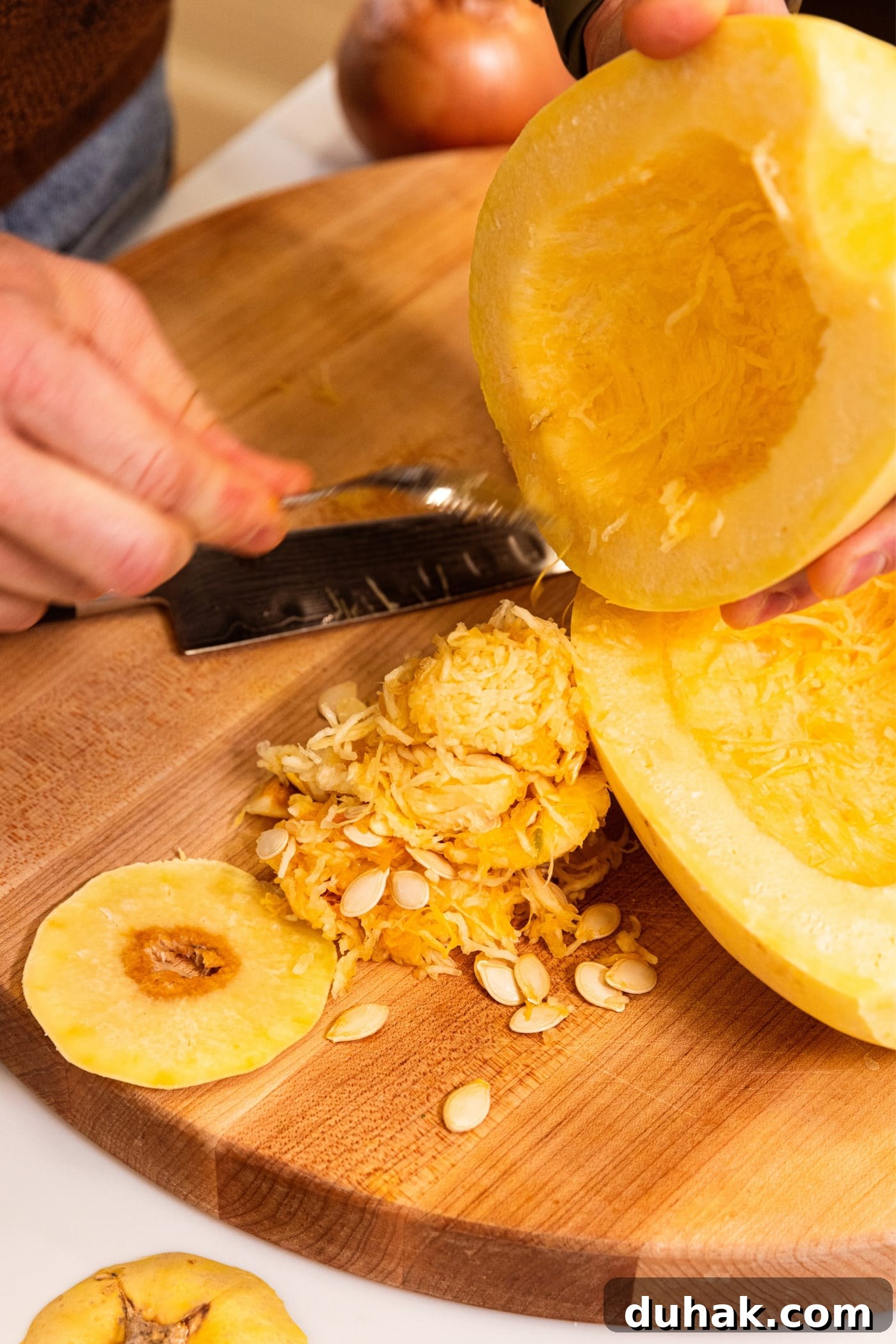 Cheesy Turkey & Spaghetti Squash Casserole Recipe 6 Hand using a spoon to scoop out the interior of a halved spaghetti squash onto a wooden cutting board.