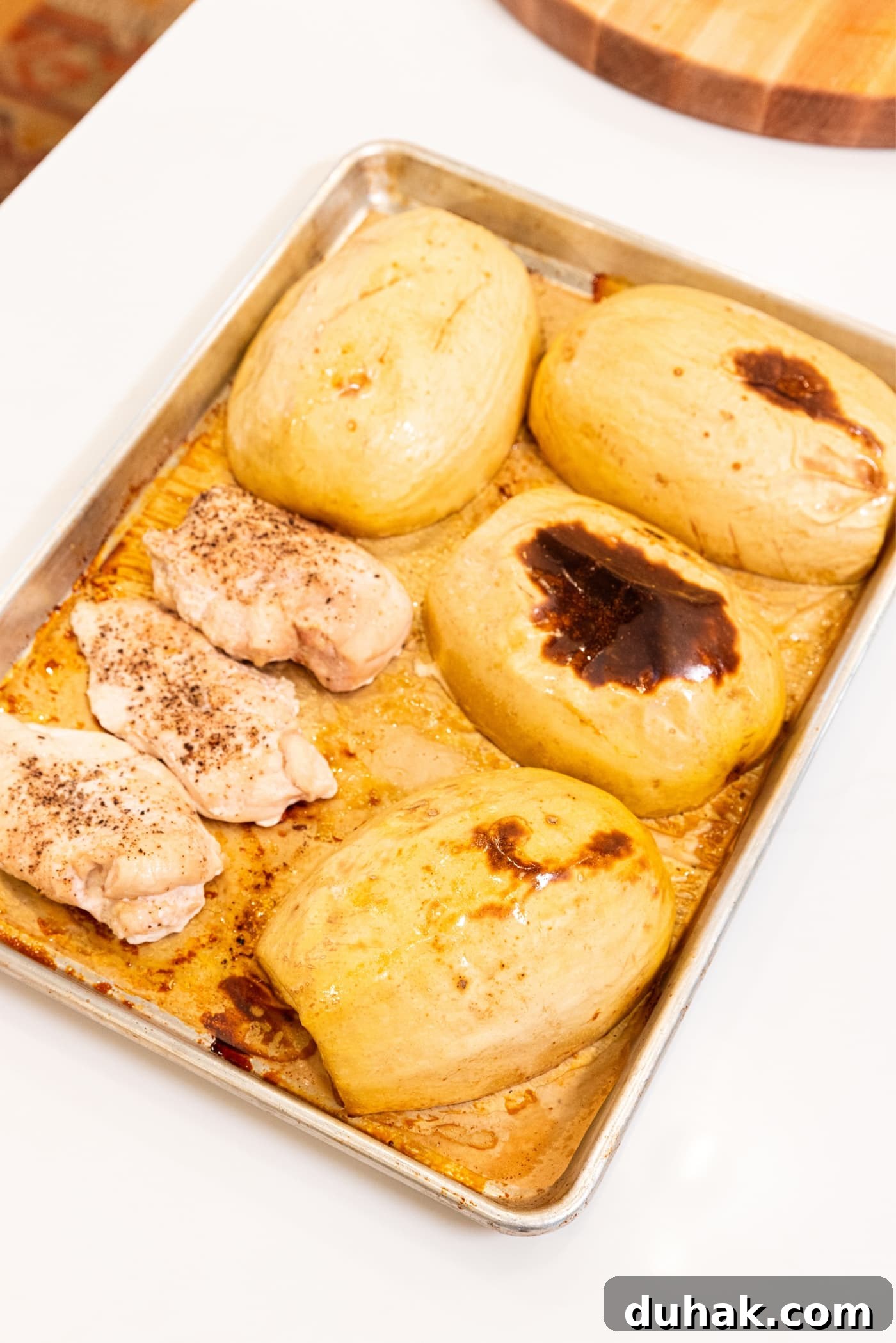 Cheesy Turkey & Spaghetti Squash Casserole Recipe 8 Parchment-lined baking sheet with roasted pieces of squash and chicken breasts with a few brown spots on top of the squash sitting on white countertop after coming out of the oven.