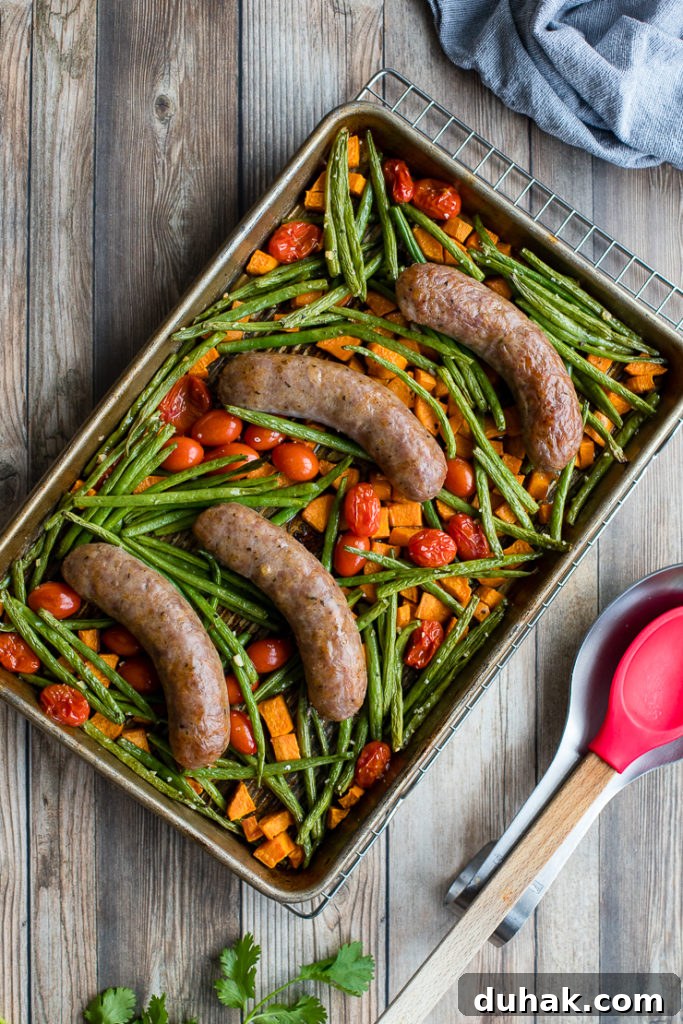 One-Pan Italian Sausage with Roasted Vegetables 8 Flat-lay of an Italian sausage sheet pan dinner with sweet potatoes, green beans, and cherry tomatoes, resting on a cooling rack with a red serving spoon to the side.