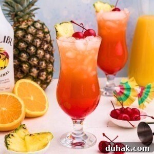 Bahama Mama Cocktail Recipe: Tropical Rum Drink Guide 13 Red and orange drink mixed together in a hurricane glass with orange slices and cherries on the marble table.