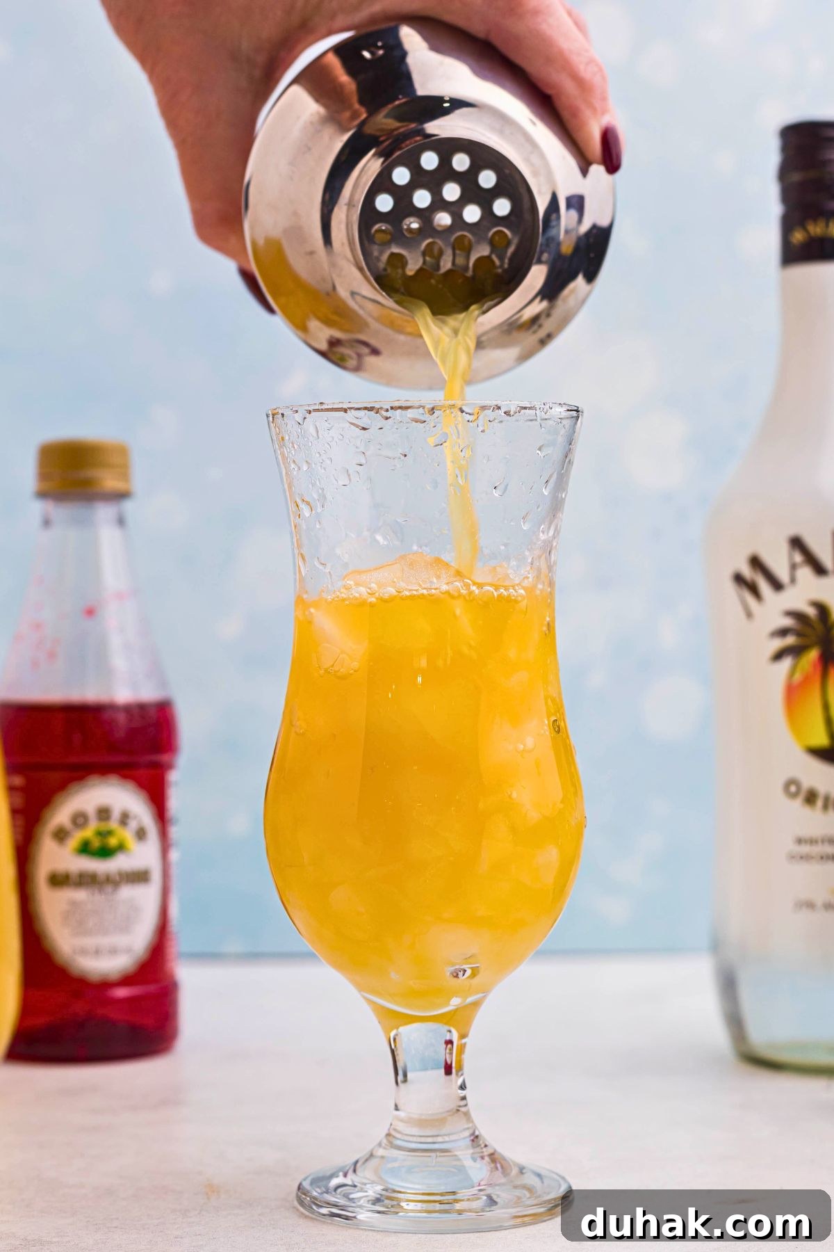 Bahama Mama Cocktail Recipe: Tropical Rum Drink Guide 5 Orange drink being poured into hurricane glass over ice, from a cocktail shaker.