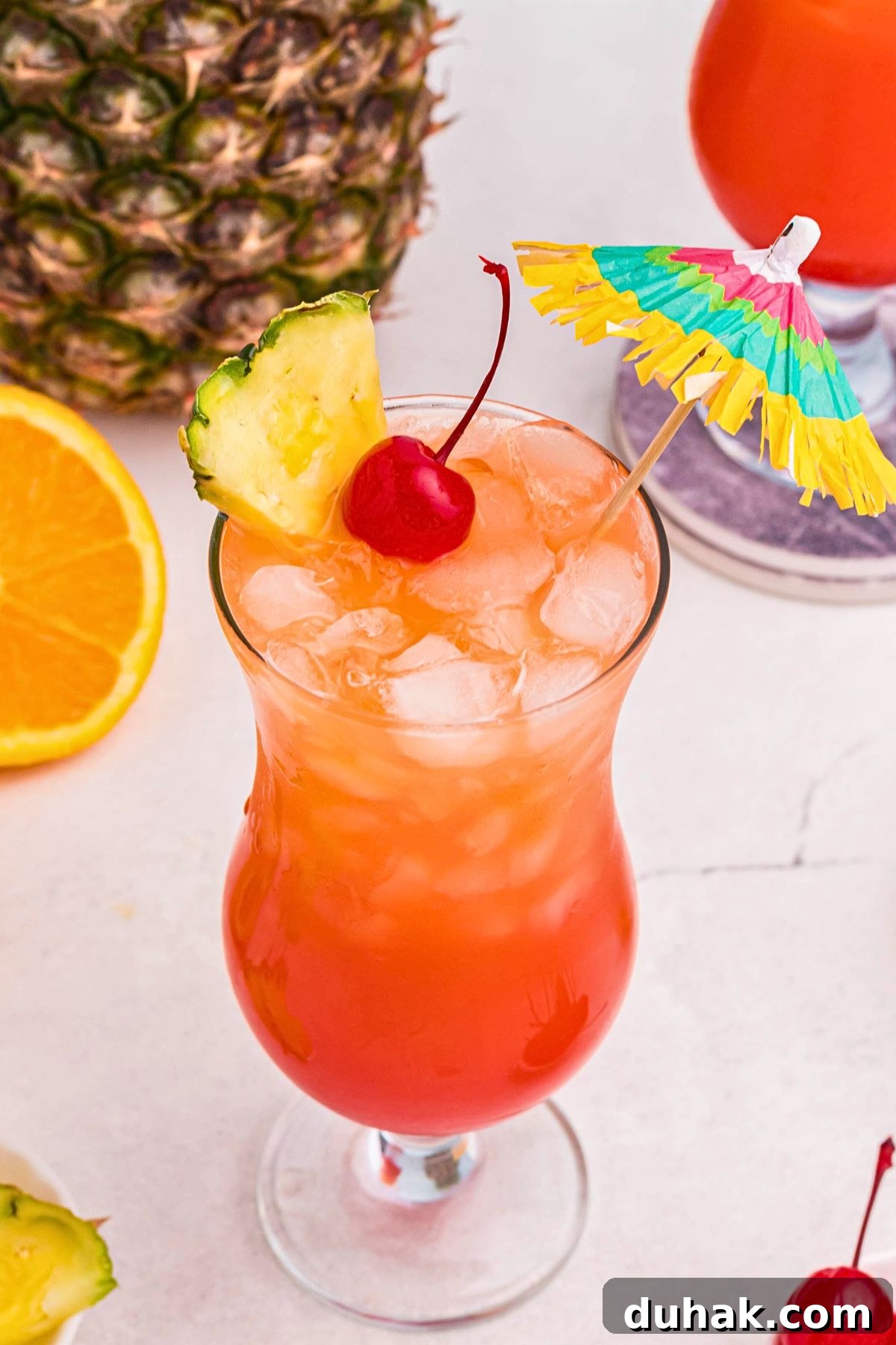 Bahama Mama Cocktail Recipe: Tropical Rum Drink Guide 7 Red and orange drink in a hurricane glass, topped with a cherry, pineapple slice, and paper umbrella.