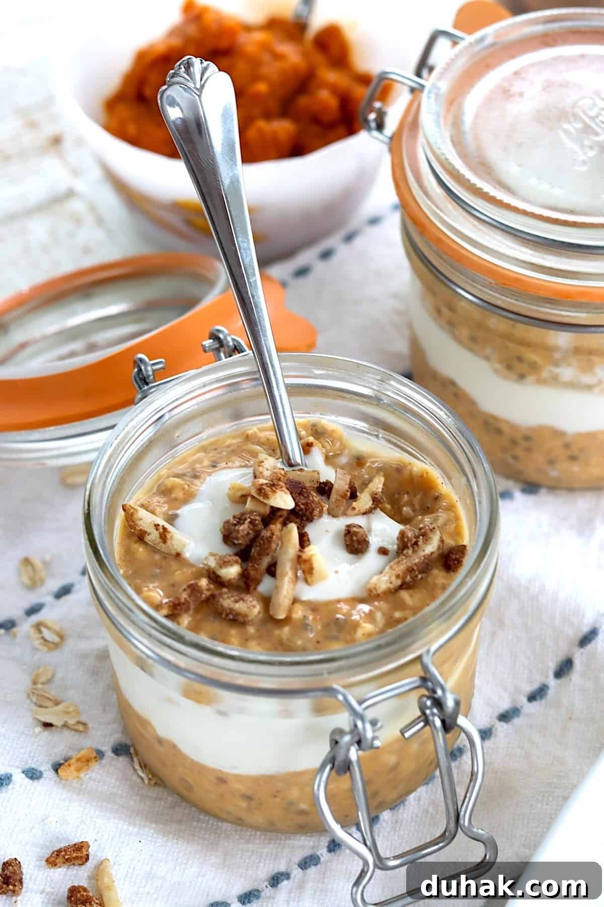 A glass jar layered with pumpkin pie overnights oats, maple yogurt swirl and topped with toasted candied almonds.