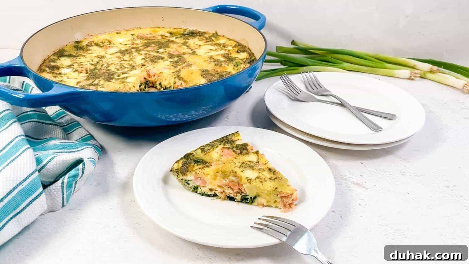 24 Low-Carb Morning Wins for Delicious, Satisfying Breakfasts 11 A slice of vegetable and cheese frittata is served on a white plate beside a blue baking dish, with stacked plates, forks, green onions, and a striped towel nearby.