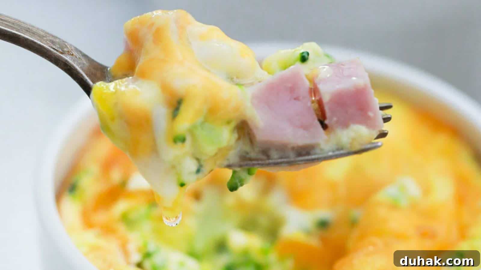 24 Low-Carb Morning Wins for Delicious, Satisfying Breakfasts 5 A fork holding a bite of mini frittata with ham and broccoli, with the dish in the background.