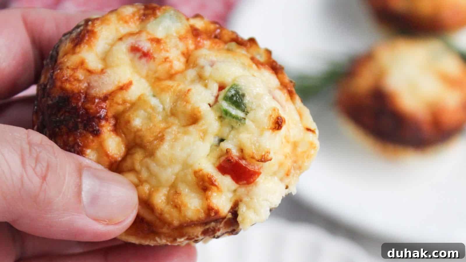 24 Low-Carb Morning Wins for Delicious, Satisfying Breakfasts 7 A close-up of a hand holding an egg white frittata muffin with visible toppings of cheese and chopped peppers.