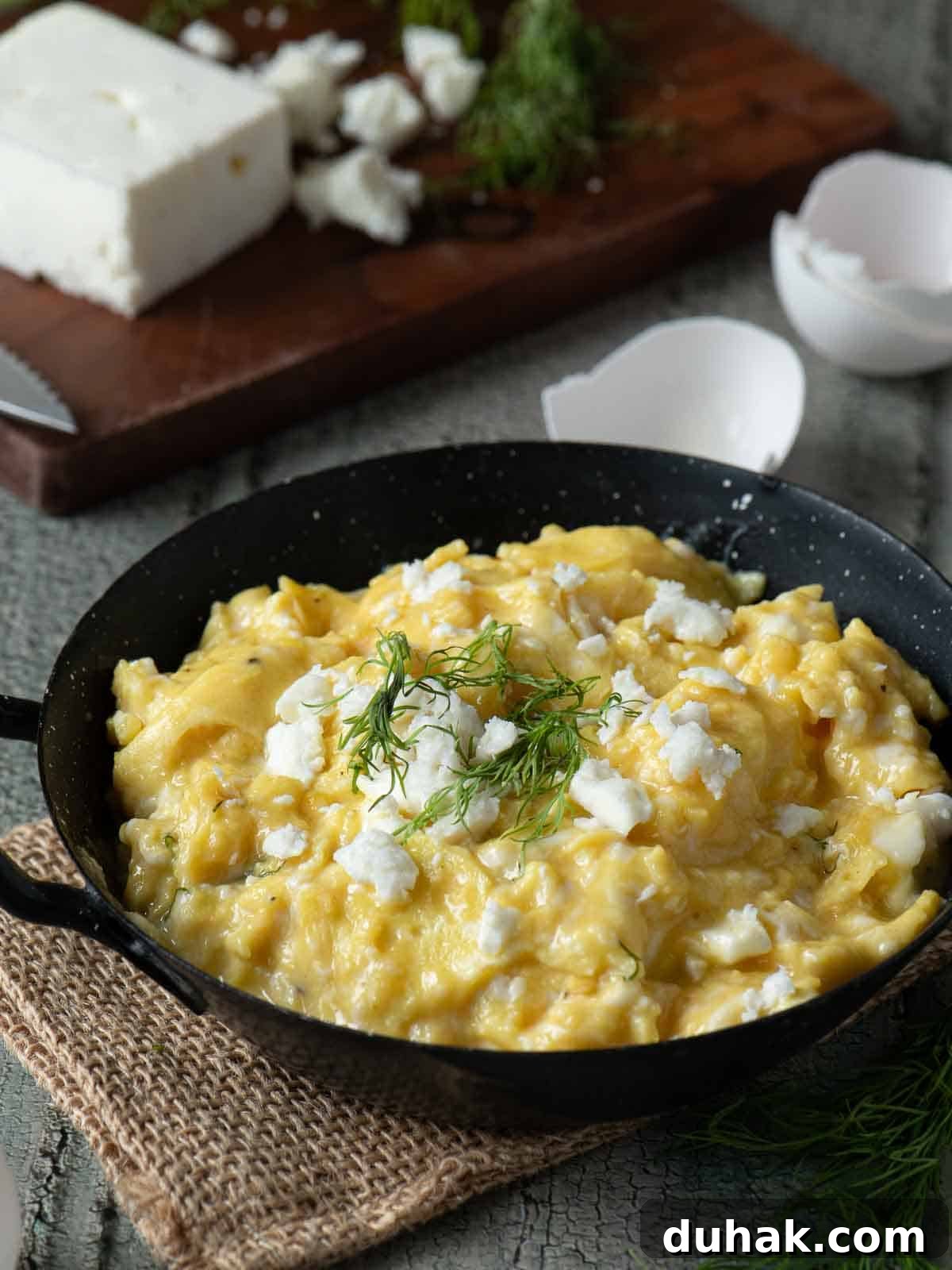 Creamy Feta and Dill Scrambled Eggs Recipe 2 Angled view of scrambled eggs in a skillet with feta on top.