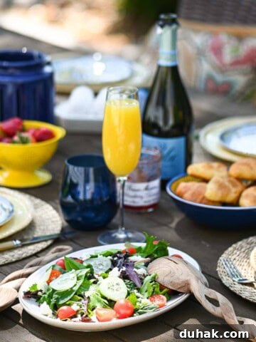 Casual outdoor brunch served on a wooden table with food and beverages in the background.