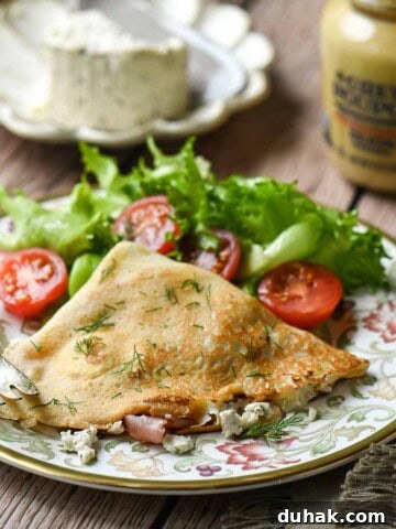 Savory crepes on a plate with a tomato and lettuce salad in the back.