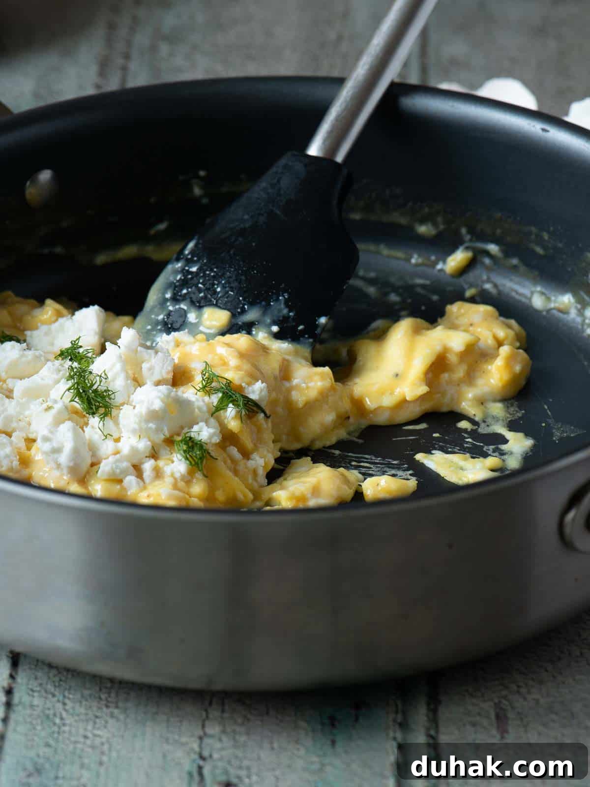 Creamy Feta and Dill Scrambled Eggs Recipe 7 Scrambled eggs being prepared in a skillet with a spatula and toppings.