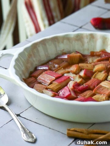 Roasted rhubarb in a white baking dish with a striped apron in the back.