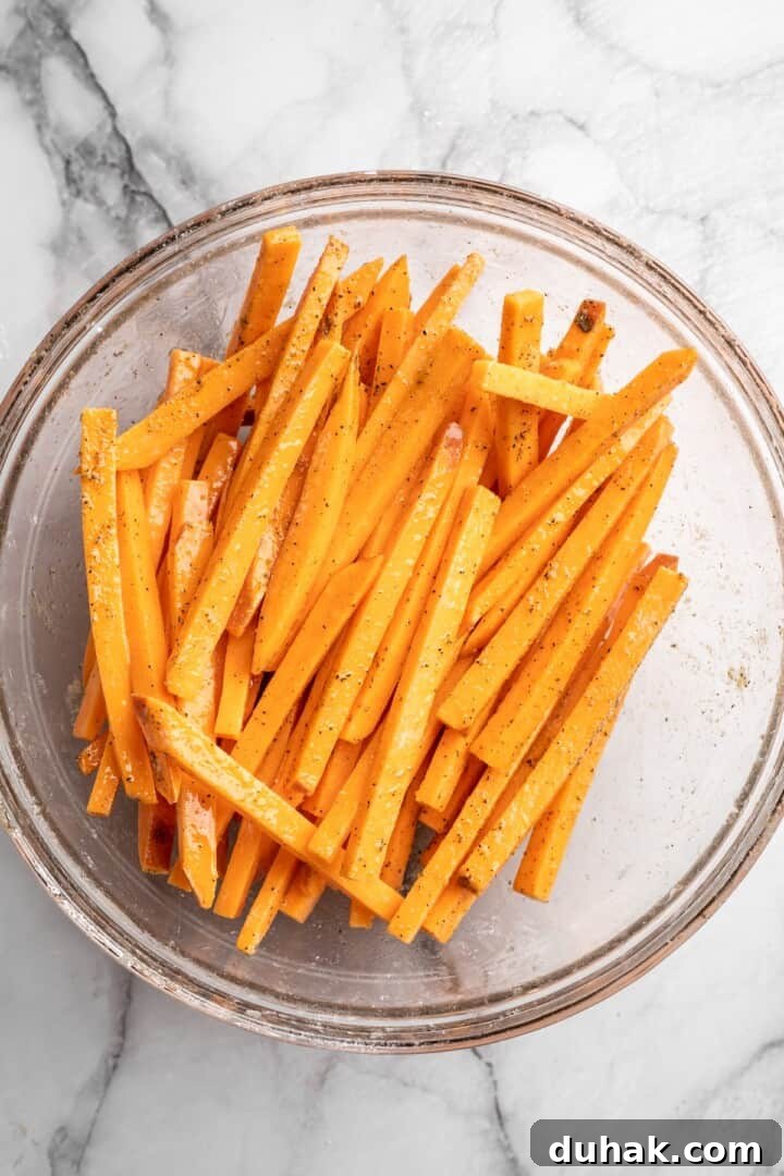 Add cornstarch, oil and seasoning Overhead view of sweet potato fries in bowl after adding oil and seasoning