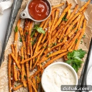 Crispy Oven-Baked Sweet Potato Fries Recipe 2 Overhead view of sweet potato fries on pan with bowls of aioli and ketchup