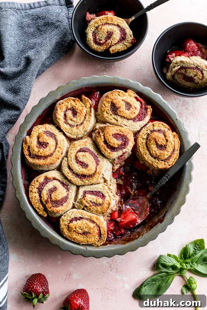 Overhead view of strawberry basil cobbler in a pie dish on a pink surface.