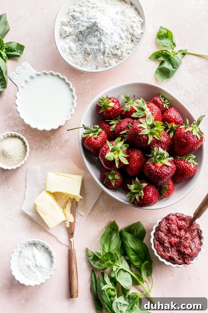 Overhead view of ingredients to make strawberry basil cobbler arranged on a pink surface.