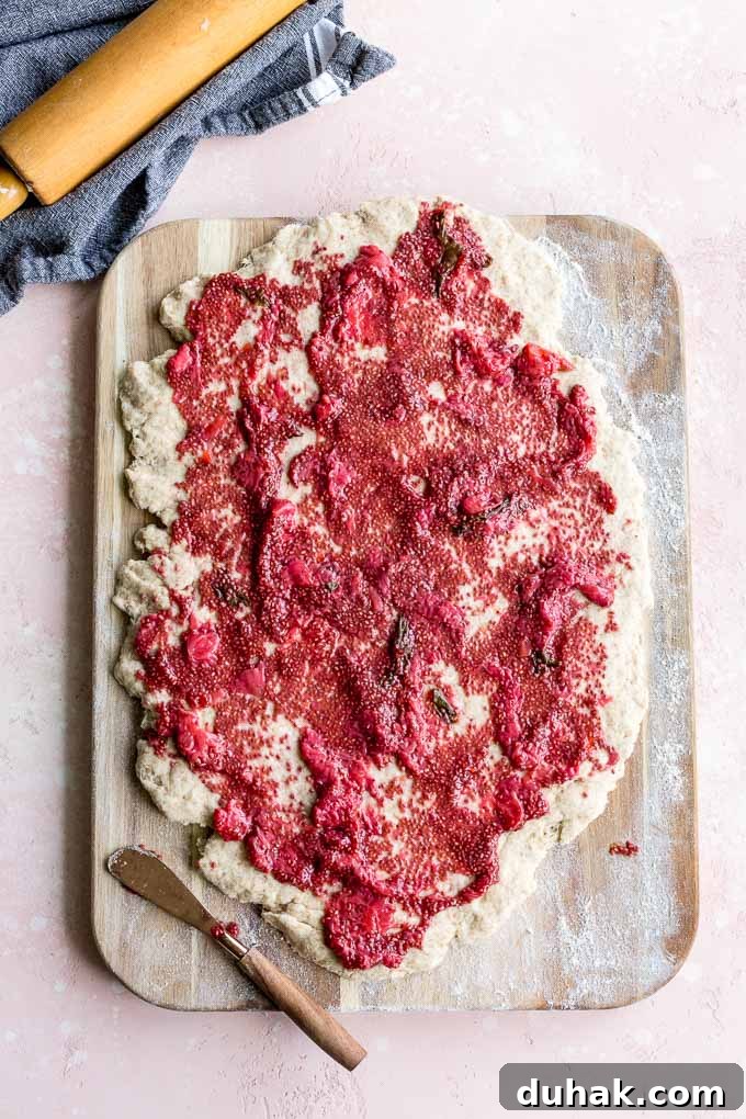 Biscuit dough rolled out on a wooden surface with jam spread out on top.