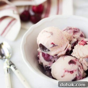 scoops of rum cherry ice cream in a white bowl next to spoons and a red and white striped napkin