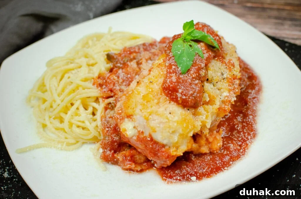 Chicken parmesan served with tomato passata sauce and spaghetti on a white plate