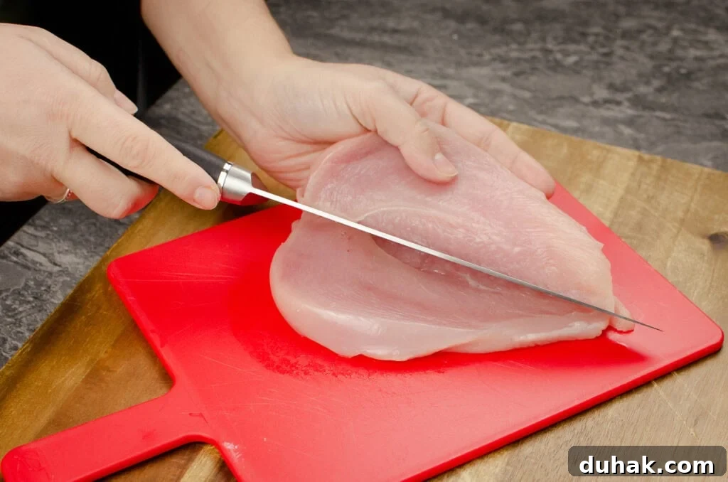 Cutting a chicken breast in half with a silver knife on a red chopping board