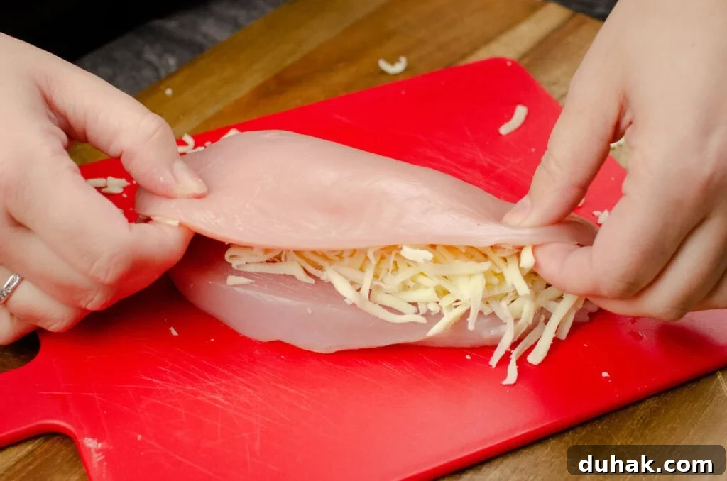 A chicken breast stuffed with grated mozzarella cheese and folded the top half of the breast over the cheese by hand on a red chopping board