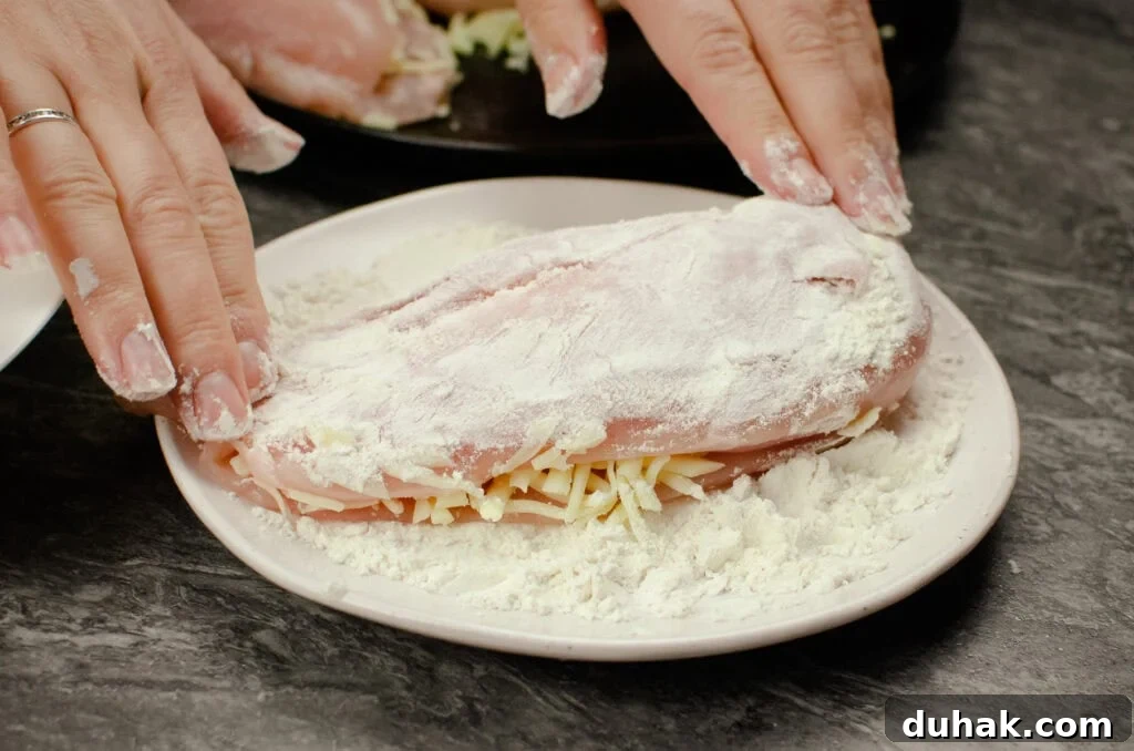 Dipping mozzarella stuffed chicken breast into flour on a white plate
