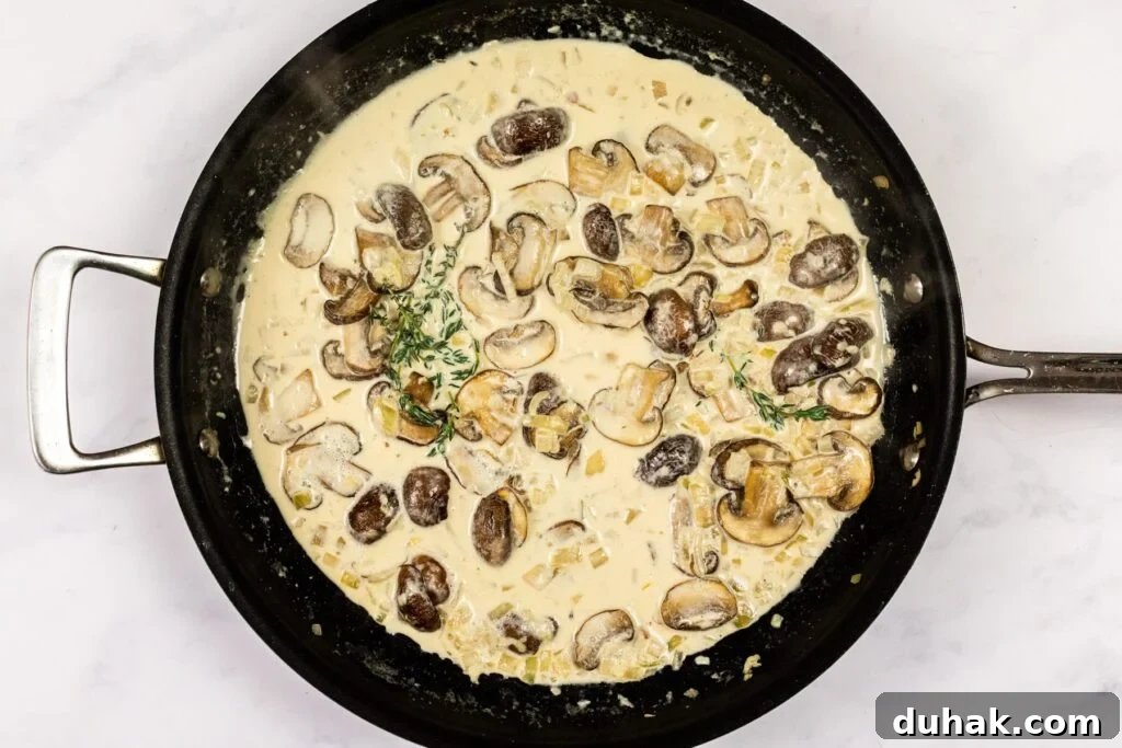 Creamy mushroom sauce reducing in a skillet.