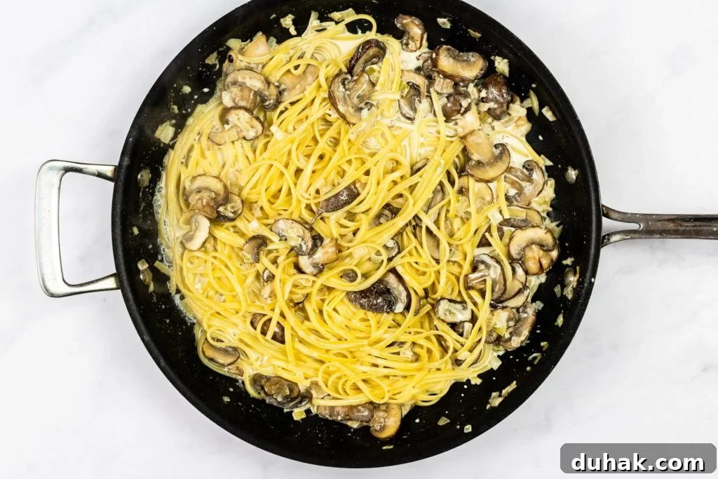 Creamy garlic mushroom pasta cooking in a skillet.