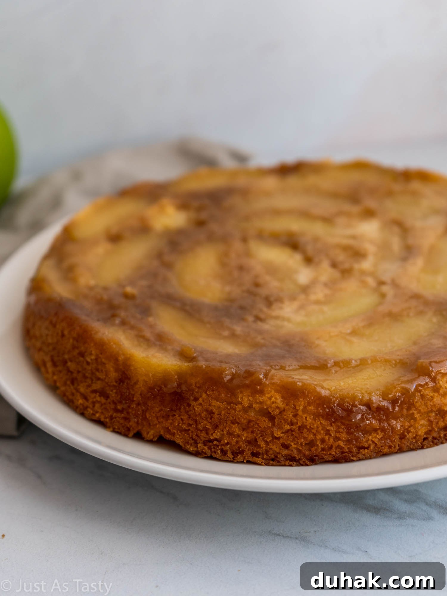 Gluten-Free Eggless Apple Cake Recipe: Moist & Simple 4 Side view of a round single-layer apple cake on a white plate.