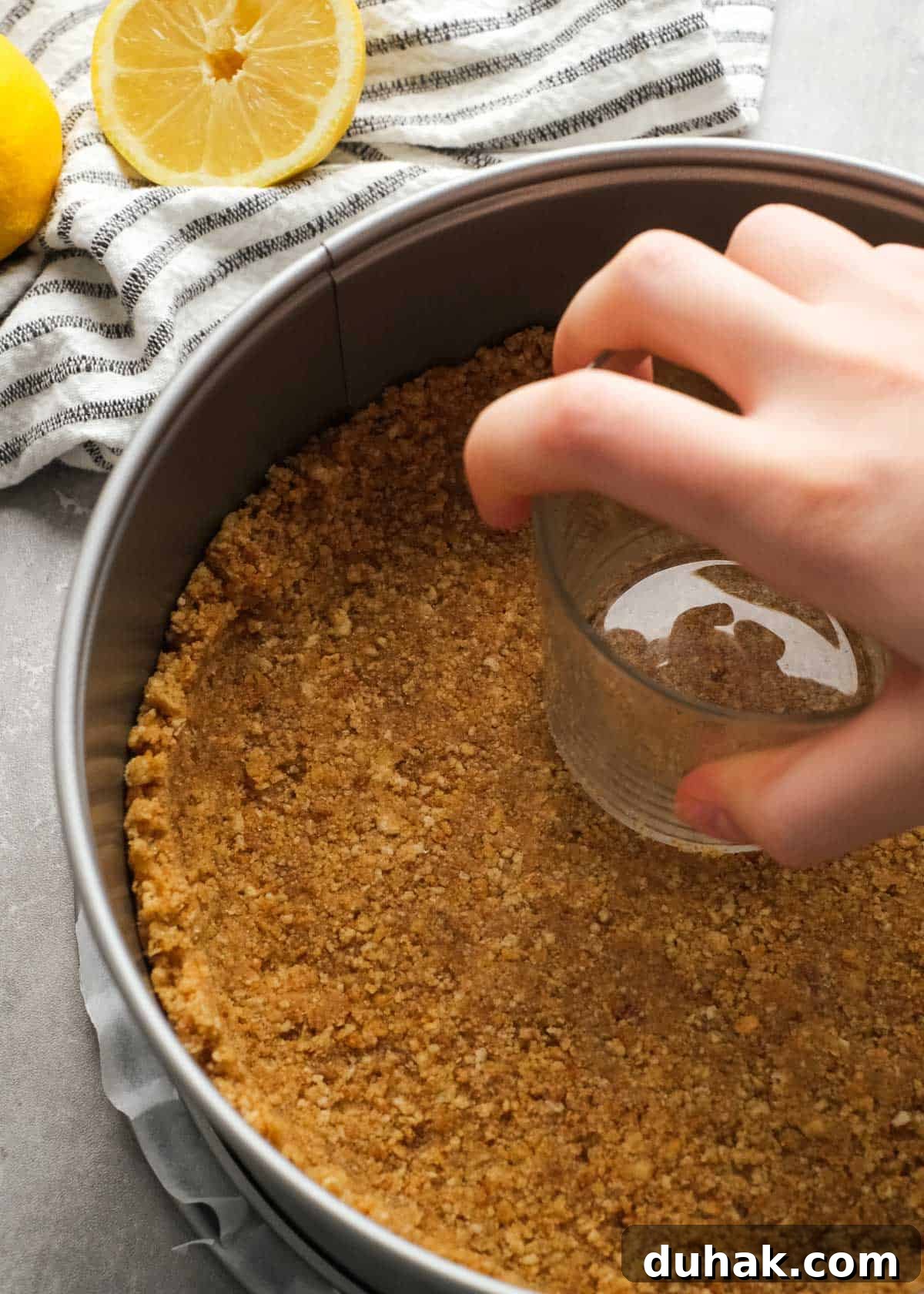 Lemon Cheesecake Recipe with Zesty Citrus Cream Filling 5 cheesecake crust being pressed into a springform pan with a glass