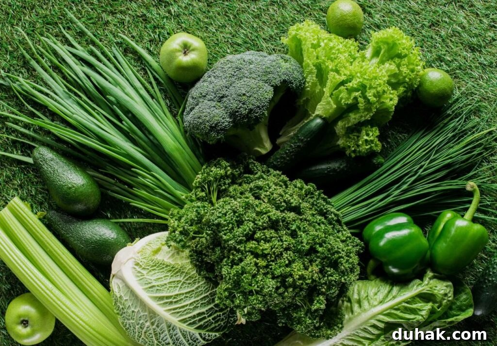 Low-Oxalate Leafy Greens to Add to Your Diet 4 A variety of green vegetables and fruits including broccoli, lettuce, apples, avocados, celery, bell peppers, and leafy greens are arranged on a grassy surface.