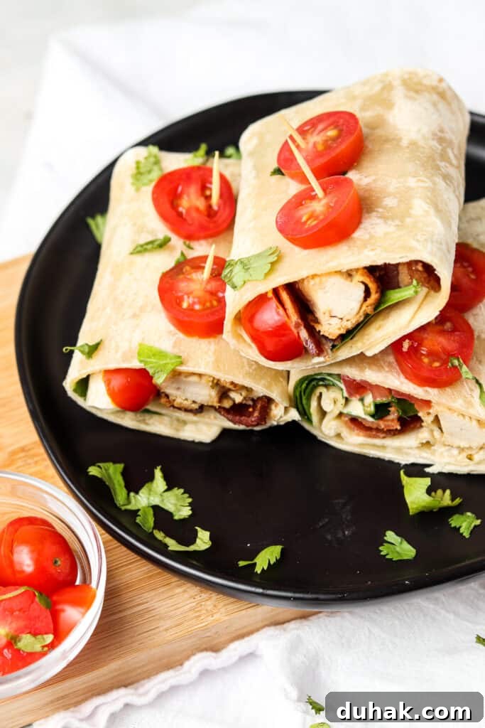 crispy bacon chicken ranch wraps on a black plate with slices of tomato held on with toothpicks