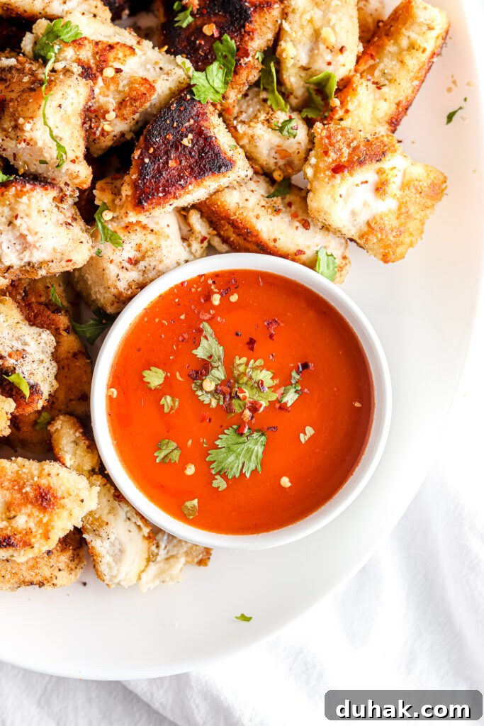 chicken nuggets with buffalo dipping sauce on a white plate with green garnish