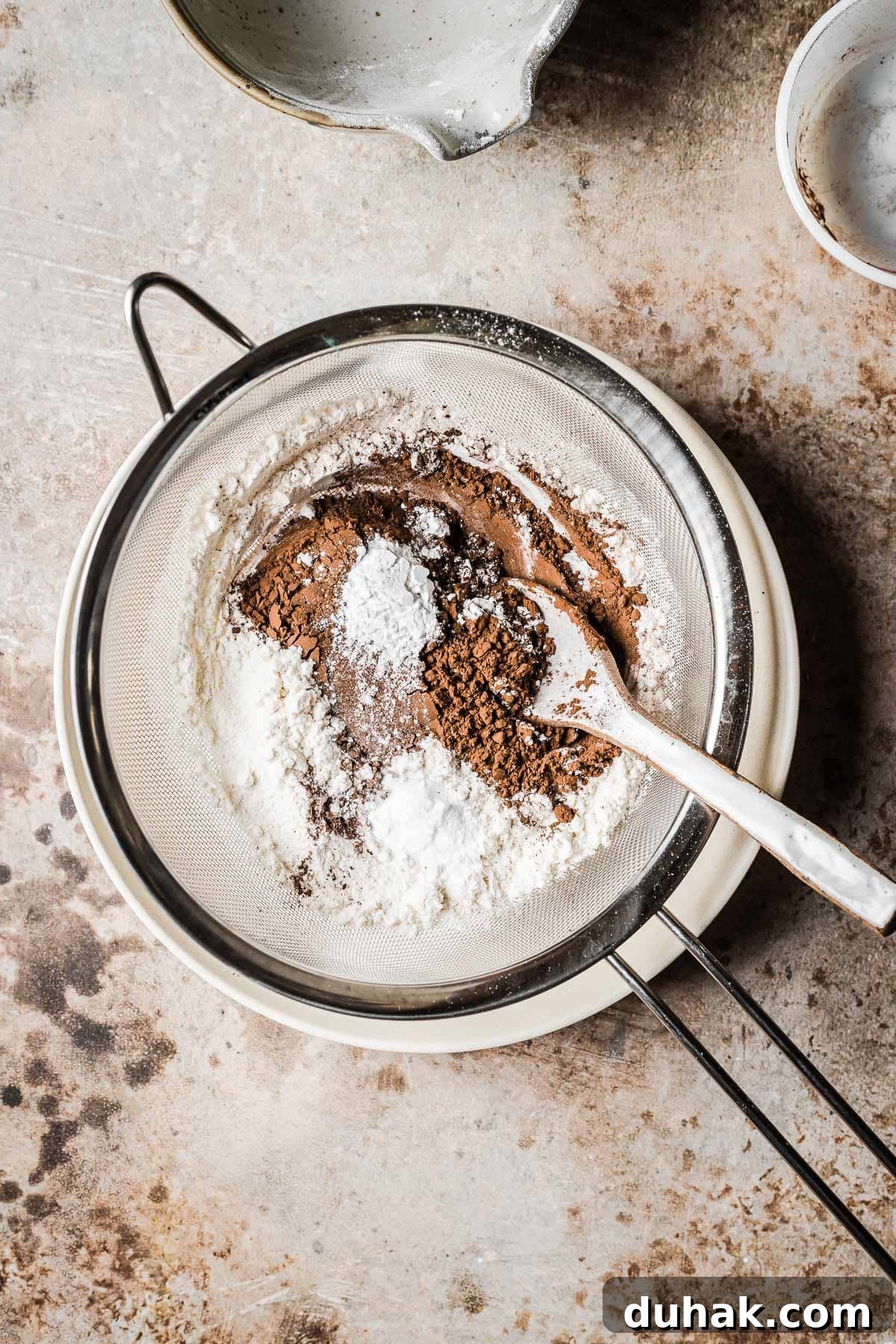 Double Cocoa Chocolate Cookies: Rich, Soft Baked Treats 4 Cocoa powder, flour and baking soda in a sieve over a tan bowl.