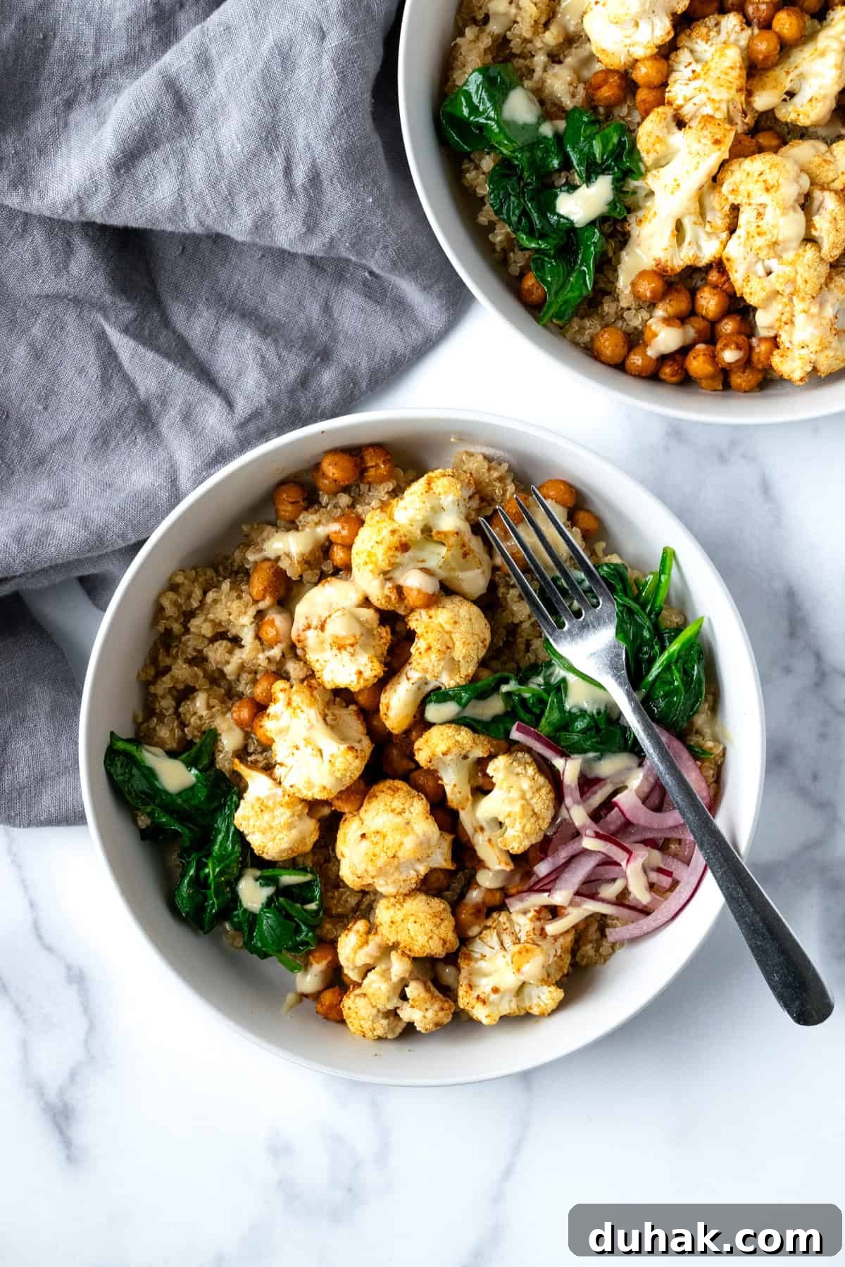 Roasted Cauliflower and Chickpeas in a white bowl with quinoa, spinach, and pickled onions.