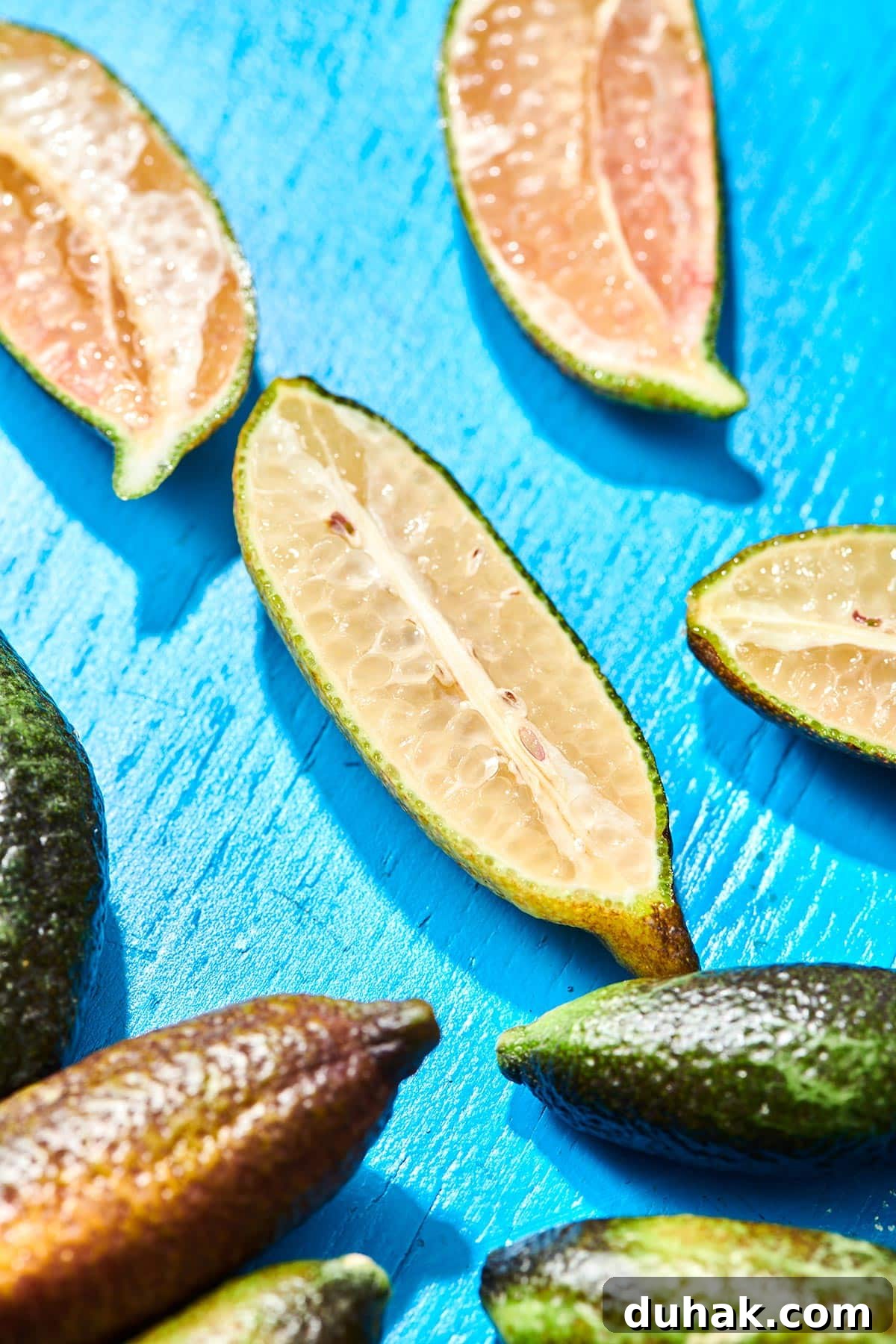 Whole and cut finger limes on blue table.