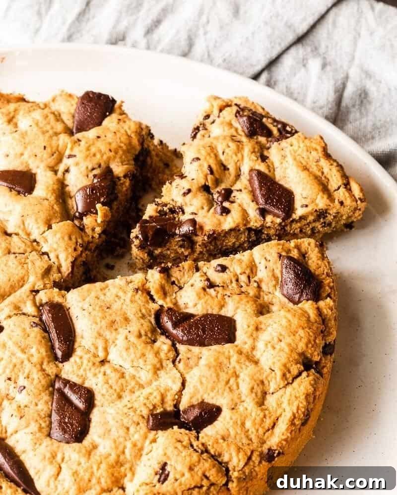 A Giant Chocolate Chip Cookie on a white plate. One slice has been cut.