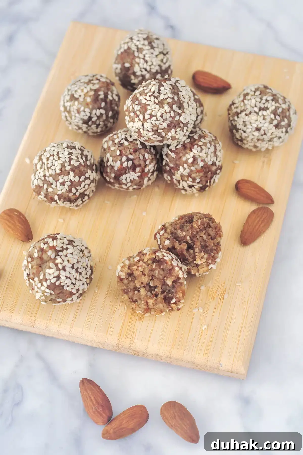 Tahini Almond Date Bites Several small round tahini date bites are arranged on a small bamboo board, with raw almonds scattered around.